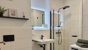Et moderne badeværelse med et glasafskærmet brusebad, en hvid vask, et toilet og en vaskemaskine.