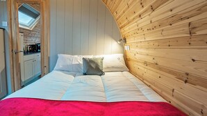 A bedroom with a bed, pillows, a red blanket, wooden walls, a skylight, and a kitchenette. - 1 bedroom accommodation in Millom (Millom)