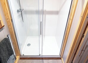Une douche fermée par des parois en verre, dotée d’une poignée en métal et d’un drain.