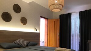 Ein Hotelzimmer mit zwei Betten, einem hölzernen Kopfteil, einer gewobenen Leuchte und Blick nach draußen durch eine Tür.