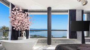 Un bagno moderno con una vasca da bagno indipendente, una grande finestra con vista sull'acqua e una TV a schermo piatto montata a parete.