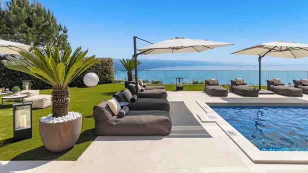 Area della piscina con un'area salotto, ombrelloni e vista sul mare.