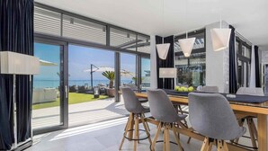 Zona pranzo moderna con vista sul mare, caratterizzata da un tavolo grande con sedie, lampade a sospensione e un divisorio in vetro.