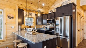 A modern kitchen with granite countertops, stainless steel appliances, and wooden cabinetry. - Rivers Retreat | Luxury New Cabin Near Gatlinburg (Sevierville)