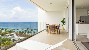 Un balcone con vista sull'oceano, un'area pranzo con sedie e tavolo, e una cucina.
