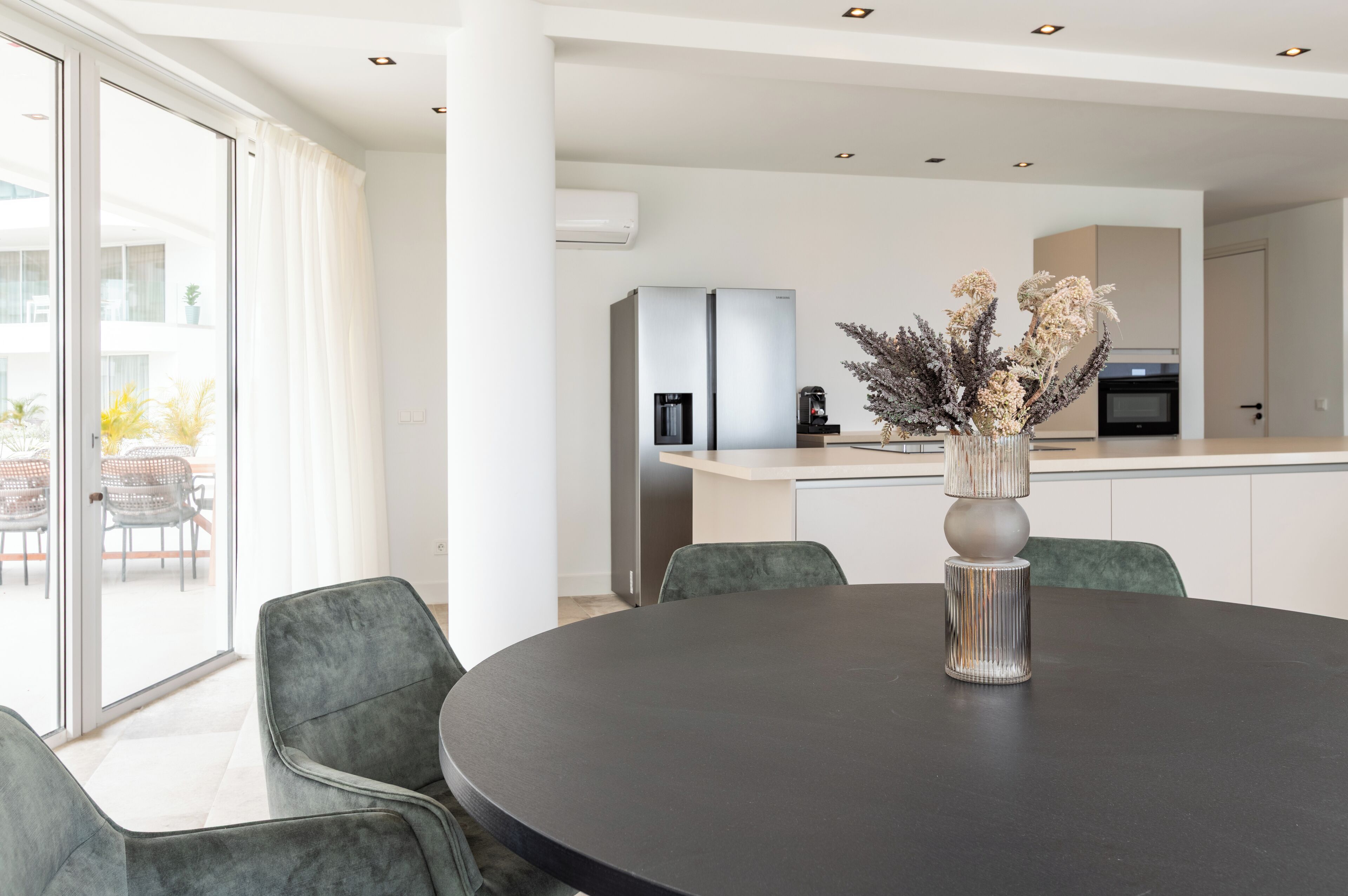 A modern dining area with a round table, grey upholstered chairs, and a decorative vase.