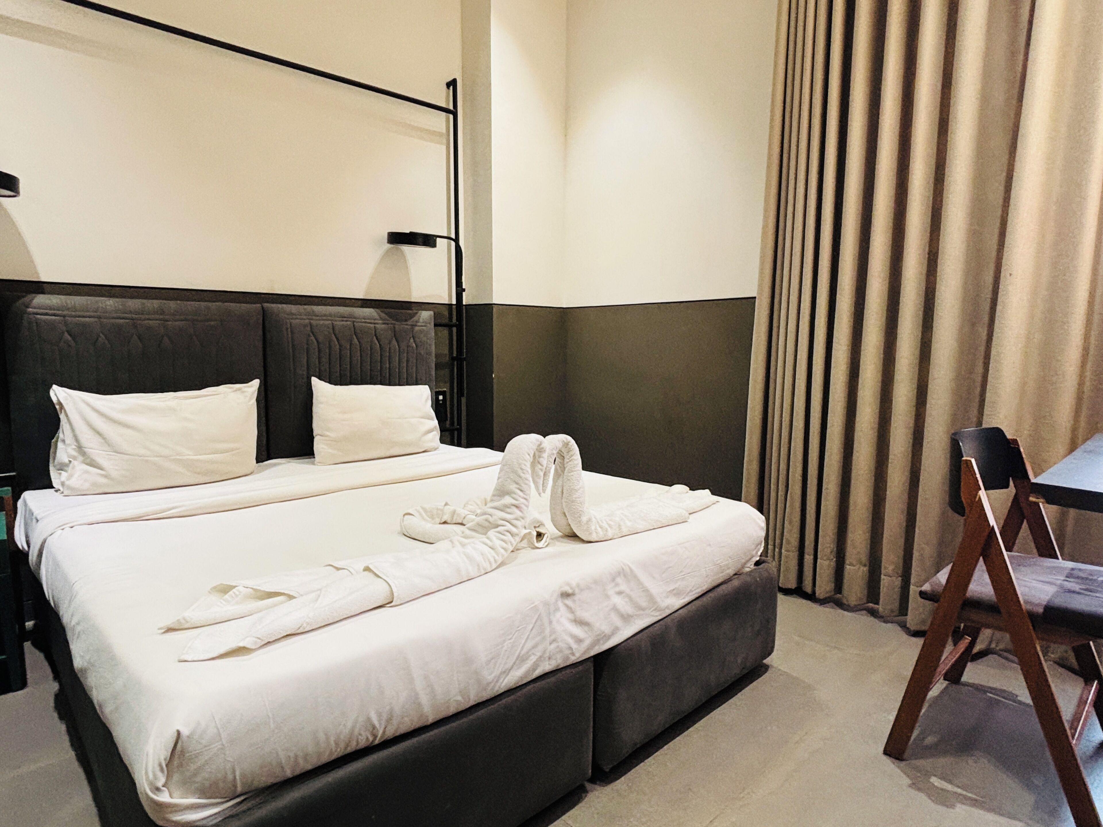 A hotel room with a large bed, a bedside table, a chair, and a curtain.