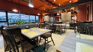 A restaurant with tables and chairs, large windows, and a view of a roller coaster.