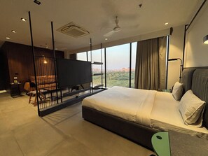 A modern hotel room with a large bed, a TV, and a balcony with a city view. - Ibiza Hotel (Ahmedabad)
