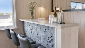 A bar area with a stone wall, bar stools, and a variety of barware including glasses, bottles, and a cocktail shaker.