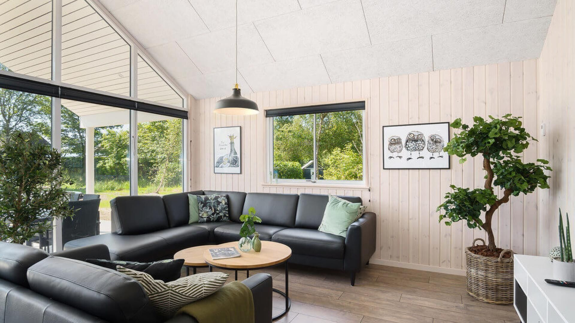 Ein modernes Wohnzimmer mit einer schwarzen Ledersofa, einem runden Couchtisch und einem großen Fenster mit Blick auf Grünflächen.