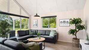 Ett modernt vardagsrum med en svart lädersoffa, ett runt soffbord och ett stort fönster med utsikt över grönområden.