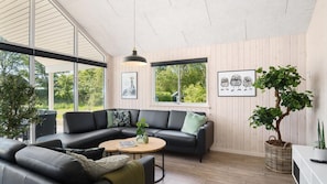 Ein modernes Wohnzimmer mit einer schwarzen Ledersofa, einem runden Couchtisch und einem großen Fenster mit Blick auf Grünflächen.