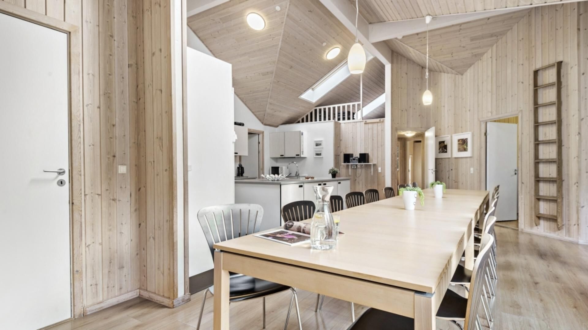 A spacious dining area with a long table, chairs, and a modern kitchen in the background.