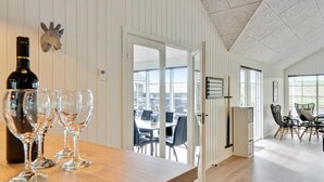 Un coin repas avec une table en bois, une bouteille de vin et des verres, une porte donnant sur un balcon et une vue sur le paysage urbain.