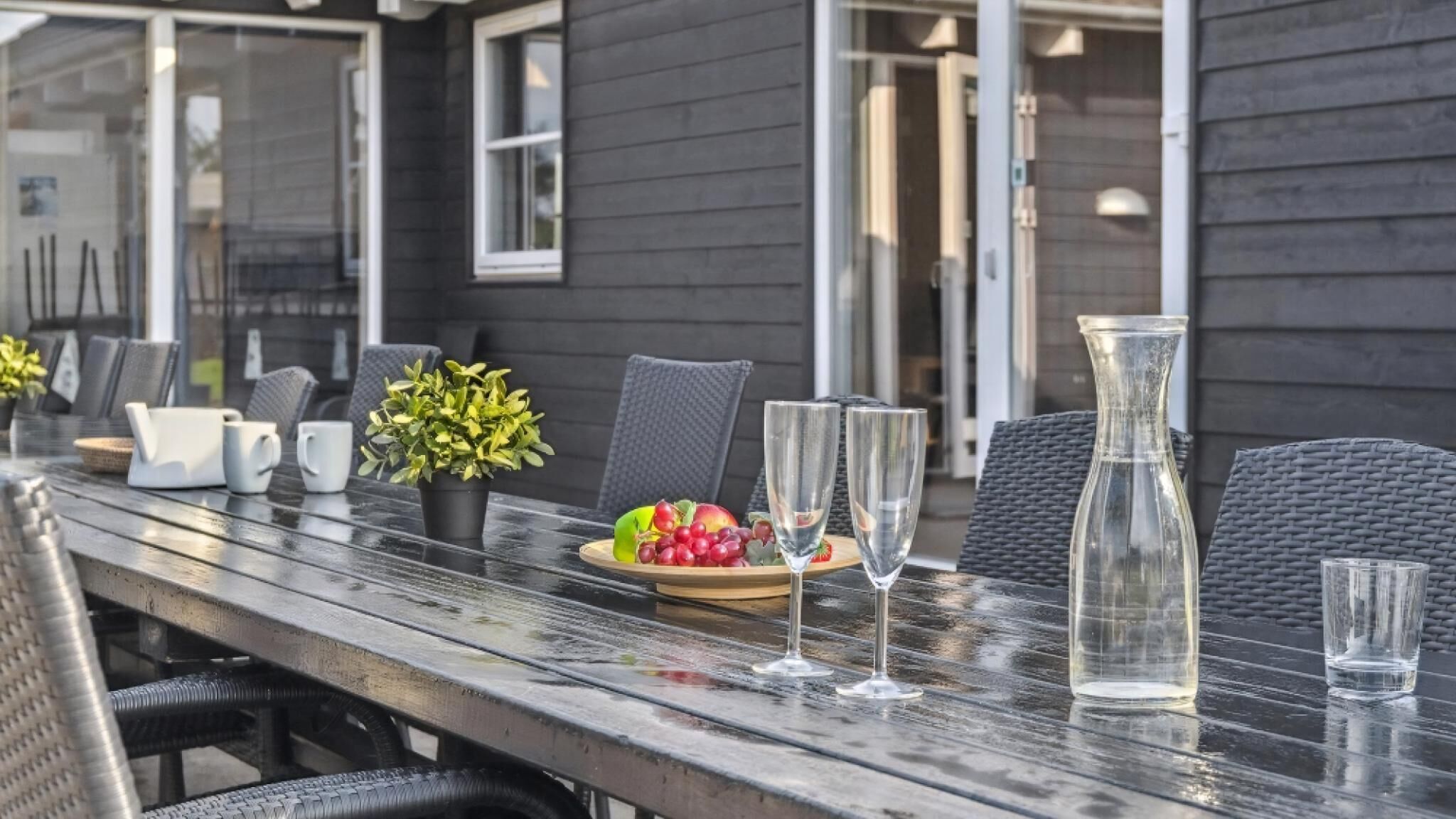 Een terras met eettafel voor twee personen, compleet met een fruitschaal, twee wijnglazen en een karaf.