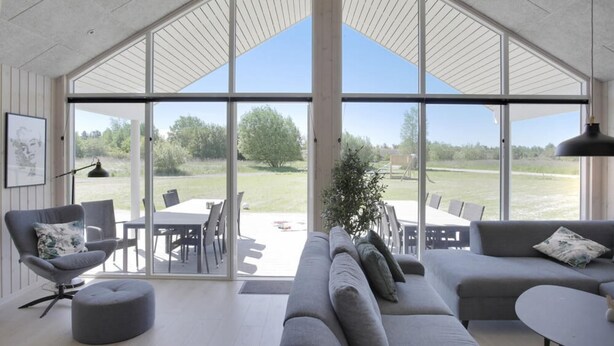 Un salon spacieux doté d’une grande fenêtre, de canapés gris, d ’une table à manger et offrant une vue sur un espace extérieur verdoyant.