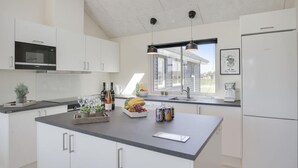 Une cuisine moderne avec des meubles blancs, un grand îlot central doté d’un plan de travail, un four à micro-ondes, un réfrigérateur et une fenêtre qui laisse entrer la lumière naturelle.