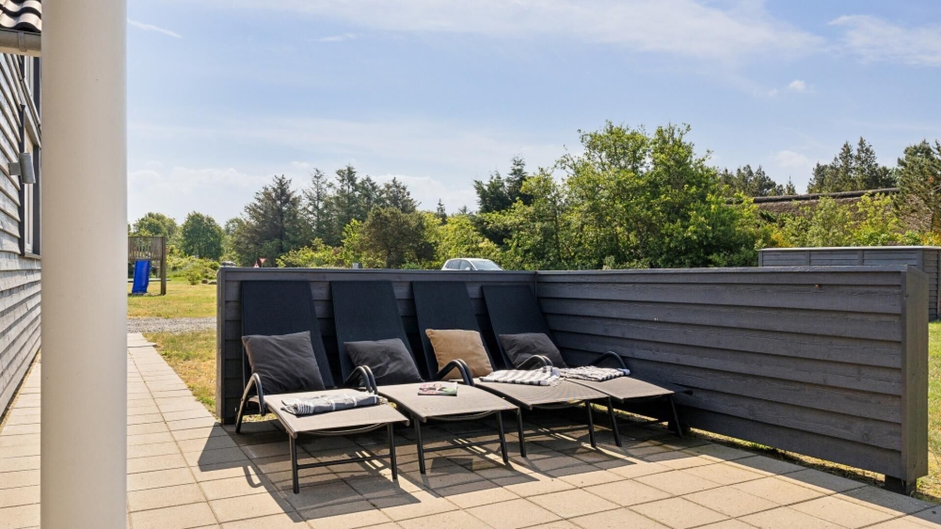 An outdoor seating area with four lounge chairs and a table, surrounded by a wooden fence and a clear sky.