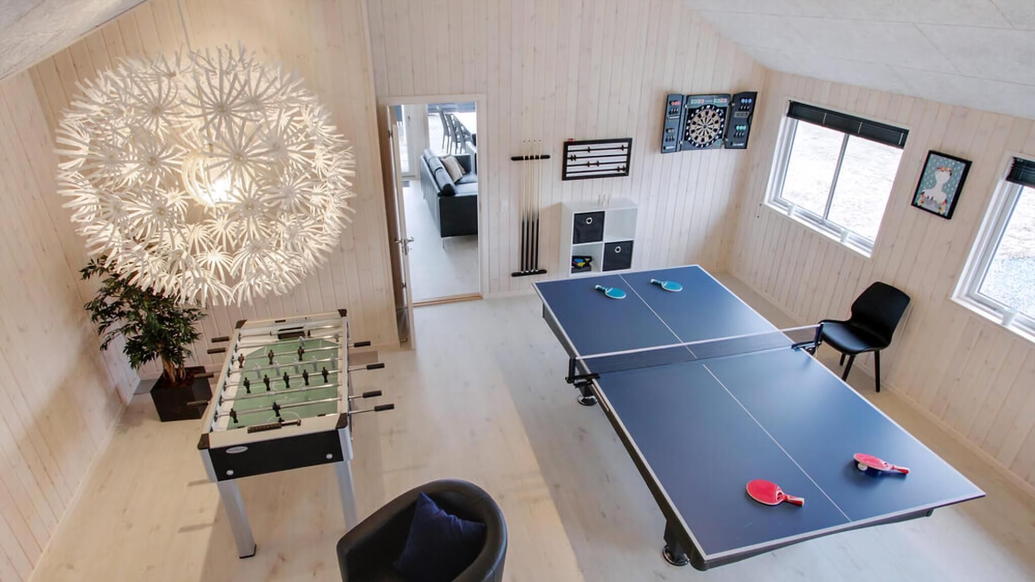 A room with a foosball table, ping pong table, and a decorative light fixture.