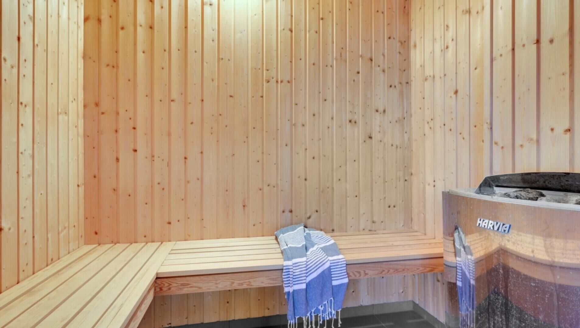 A sauna with wooden walls and benches, a towel, and a Harvia sauna heater.