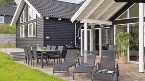 Ein modernes Haus mit einer Terrasse, die Gartenmöbel und einen Grill beinhaltet.