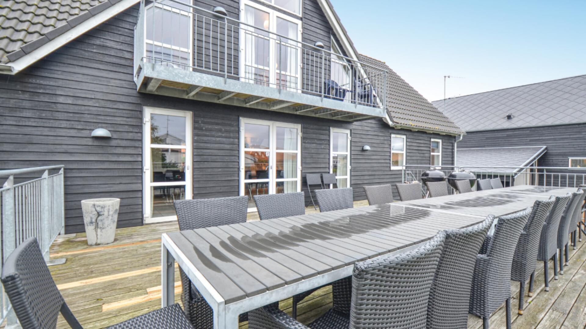 A two-story building with a balcony, a large outdoor dining area with wicker furniture, and a wooden deck.