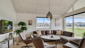 Ein modernes Wohnzimmer mit einer Eckcouch, einem runden Couchtisch, einer Topfpflanze und einem großen Fenster mit Blick ins Freie.