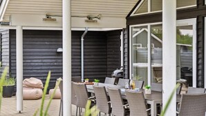 Une terrasse extérieure avec des chaises et une table en osier, un barbecue et un espace abrité doté d’une porte coulissante.