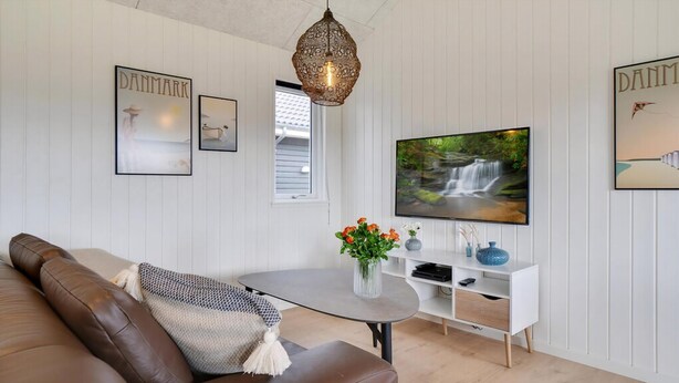 Un salon avec un canapé en cuir marron, une table basse blanche, un téléviseur posé sur un meuble blanc et des tableaux encadrés accrochés au mur.