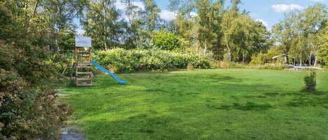 A grassy outdoor area with a wooden play structure and a blue slide.