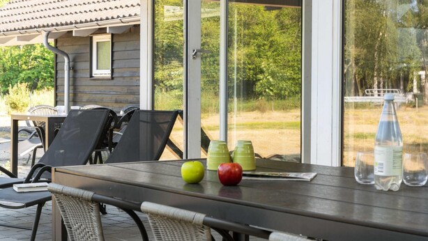 Une table avec des chaises, une fenêtre donnant sur un paysage verdoyant et une bouteille d’eau.