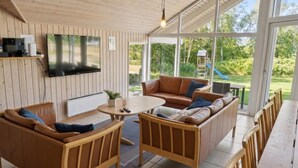 Un salon confortable avec un téléviseur, un canapé et une table à manger, donnant sur un jardin équipé d’un toboggan.