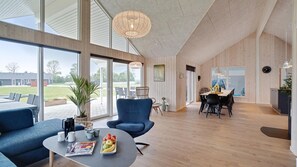 A spacious living area with a large window, a dining table, and blue chairs. - VillaVilla 472 - Grenå Strand, Østjylland (Grenaa)