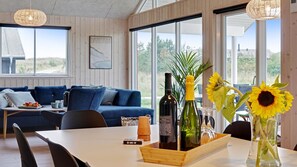 A modern living room with a blue sofa, a dining table with a bottle of wine, and a vase with sunflowers. - VillaVilla 472 - Grenå Strand, Østjylland (Grenaa)