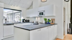 A modern kitchen with white cabinetry, a large island, and a built-in microwave. - VillaVilla 515 - Marielyst, Lolland/Falster/møn (Væggerløse)