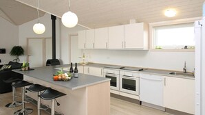 Una cocina moderna con armarios blancos, una isla central con taburetes de bar, horno empotrado y una ventana sobre el fregadero.