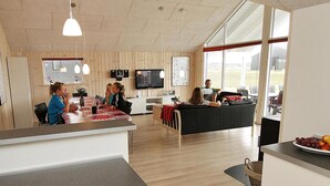 Moderni keittiö, jossa on puuseinät, ruokailutila pöytineen ja tuoleineen sekä olohuone, jossa on sohva ja televisio.
