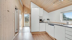 Een moderne keuken met witte kasten, een inbouwoven en een raam met uitzicht op een natuurlandschap.