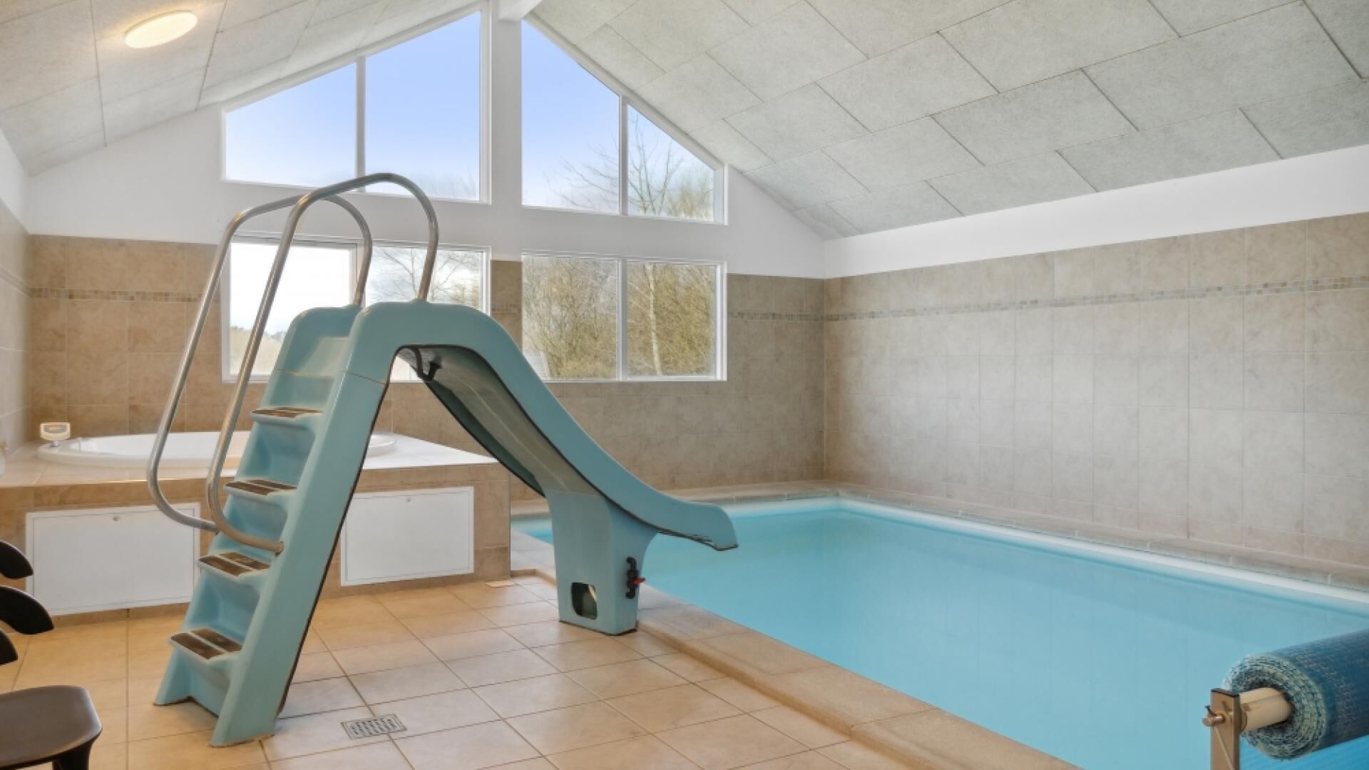 Une piscine avec un toboggan, un banc et une fenêtre laissant entrer la lumière naturelle.