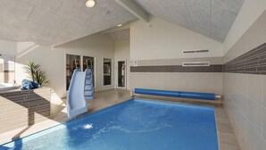 Una piscina con uno scivolo, una zona soleggiata con una panchina e una porta che dà su un'altra stanza.