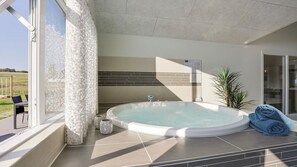 Ein moderner Wellnessbereich mit Whirlpool, Glastür zum Außenbereich und Blick ins Freie.
