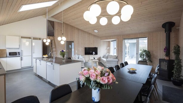 Een moderne keuken met witte kastjes, een magnetron en een spoelbak. Er is een eethoek met een tafel en stoelen, en een tv aan de muur bevestigd.