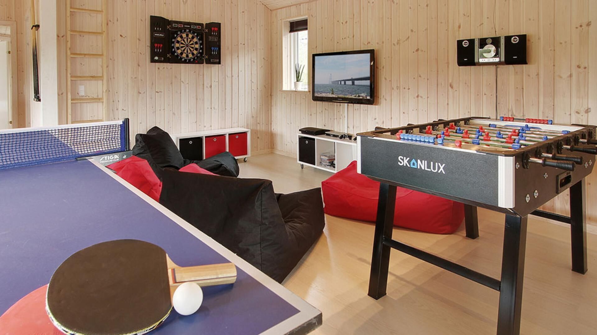 Una sala recreativa con mesa de fútbolín, mesa de ping pong, dardos y televisor.