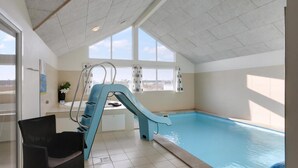 Ein Hallenbad mit blauer Rutsche, großen Fenstern und einem Stuhl in der Nähe des Beckens.