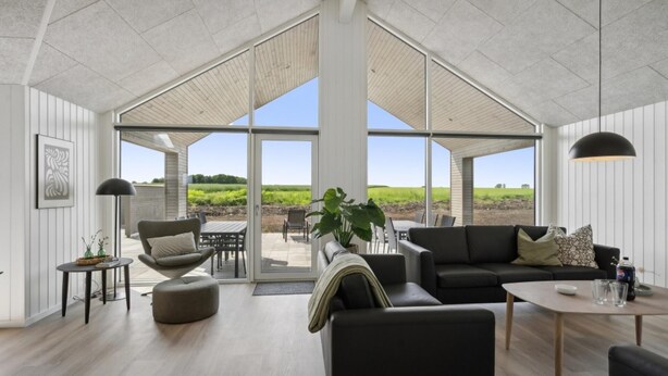 A spacious living area with a large sliding glass door leading to an outdoor patio, a black sofa, a coffee table, and a dining table. - VillaVilla 614 - Hasmark Strand, Fyn og øer (Otterup)