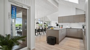 A modern kitchen with a central island, wooden flooring, and a dining area with a view of the outdoors. - VillaVilla 614 - Hasmark Strand, Fyn og øer (Otterup)