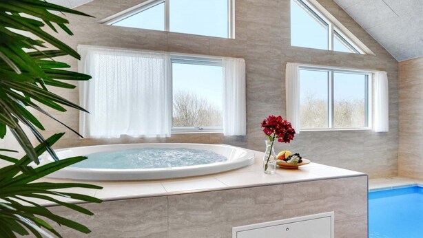 Un espace détente avec un jacuzzi, une petite table agrémentée de fruits et de fleurs, et une vue sur l’extérieur grâce à de grandes fenêtres.