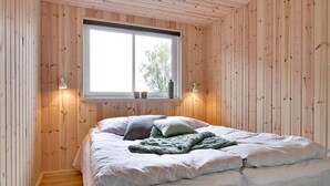 A bedroom with a large window, wooden walls, a bed with white bedding, and two wall-mounted lamps. - VillaVilla 265 - Kegnæs, Sydjylland (Sydals)