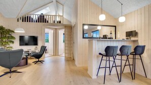 A modern interior with a wooden floor, a TV, a dining area with bar stools, and a staircase leading to an upper level. - VillaVilla 529 - Nr. Lyngby ved Løkken, nordjyllan (Løkken)